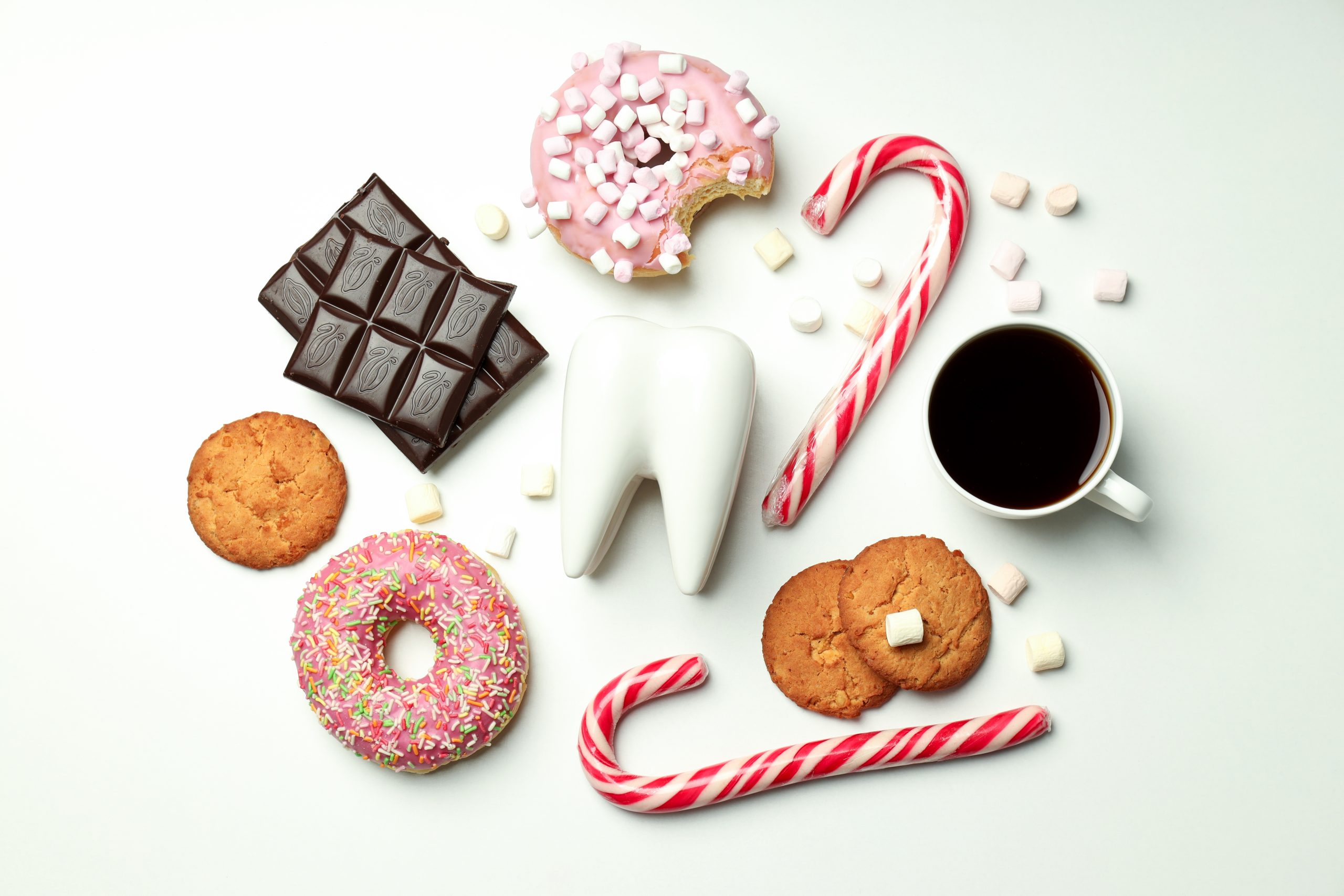 Diente en fondo blanco rodeada de donuts, chocolate, galletas y caramelos.